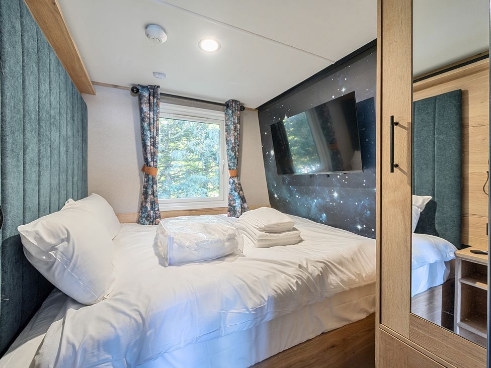 A bedroom with a bed and folded towels a window with curtains a wall-mounted TV and a wardrobe with a mirror at Skylight Stargazer - Billing Aquadrome Holiday Park