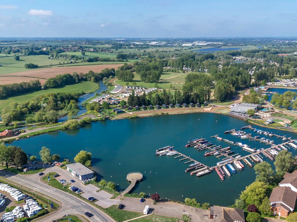 A marina with boats docked on a lake surrounded by greenery roads and buildings at Brookside Bliss - Billing Aquadrome in Billing Aquadrome Holiday Park