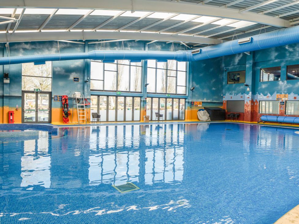 An indoor swimming pool with large windows chairs lifeguard equipment and blue and orange walls at Brookside Bliss - Billing Aquadrome