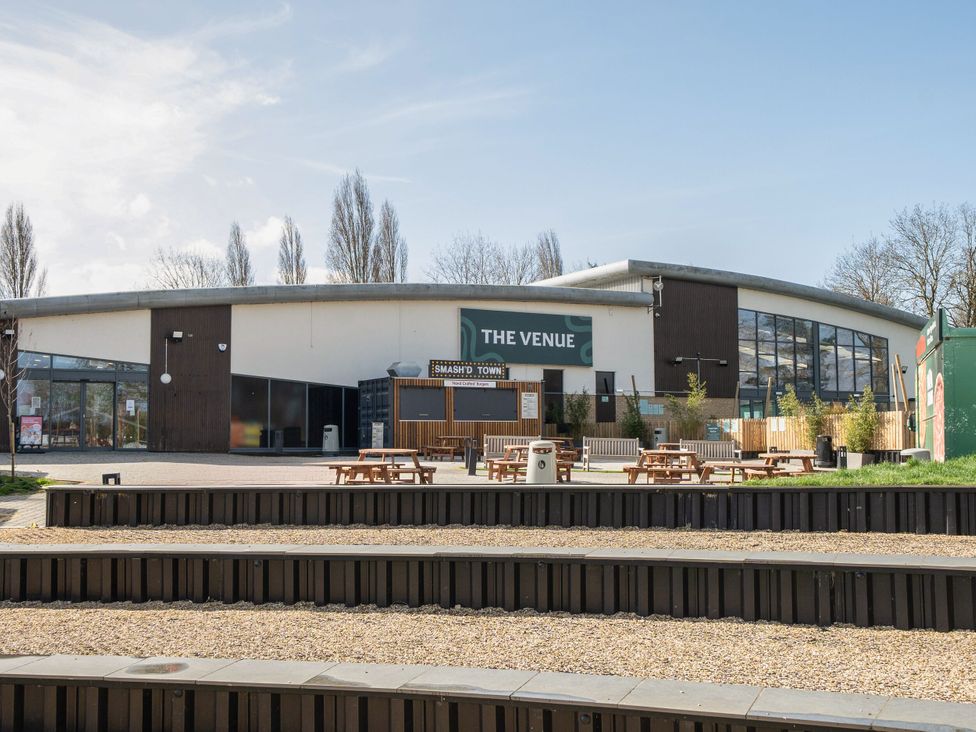 An outdoor seating area with picnic tables in front of a building labeled the venue at Billing Aquadrome Holiday Park