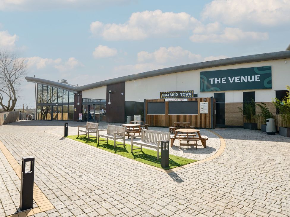 An outdoor seating area with benches and picnic tables in front of a building with signs saying The Venue and Smash'd Town at Billing Aquadrome Holiday Park