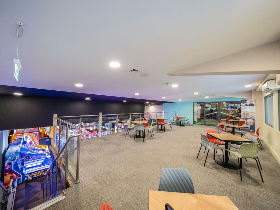 An indoor seating area with tables and chairs overlooking an arcade with games at Brookside Bliss - Billing Aquadrome in Billing Aquadrome Holiday Park
