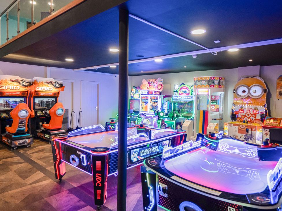 An arcade room with air hockey tables racing game machines and other neon-lit arcade games at Brookside Bliss - Billing Aquadrome