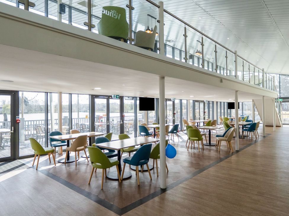 A dining area with tables and colorful chairs near large windows showing an outside deck at Brookside Bliss - Billing Aquadrome in Billing Aquadrome Holiday Park