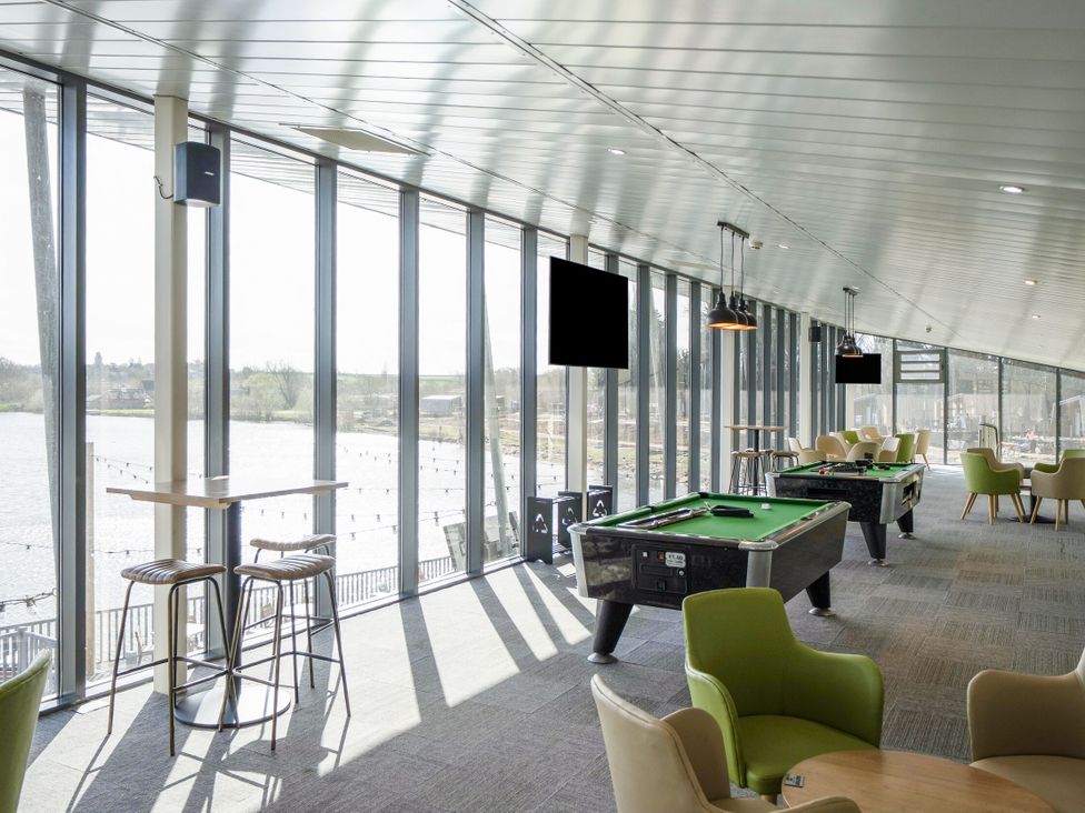 A room with pool tables green armchairs high tables and stools with large windows overlooking water at Brookside Bliss - Billing Aquadrome