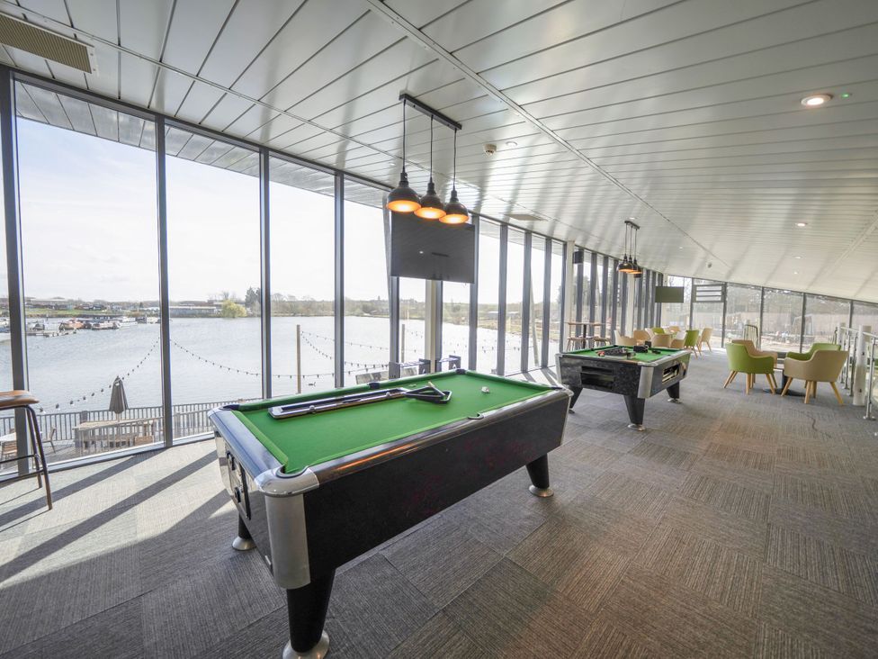 A game room with pool tables and seating by large windows overlooking a body of water at Brookside Bliss - Billing Aquadrome