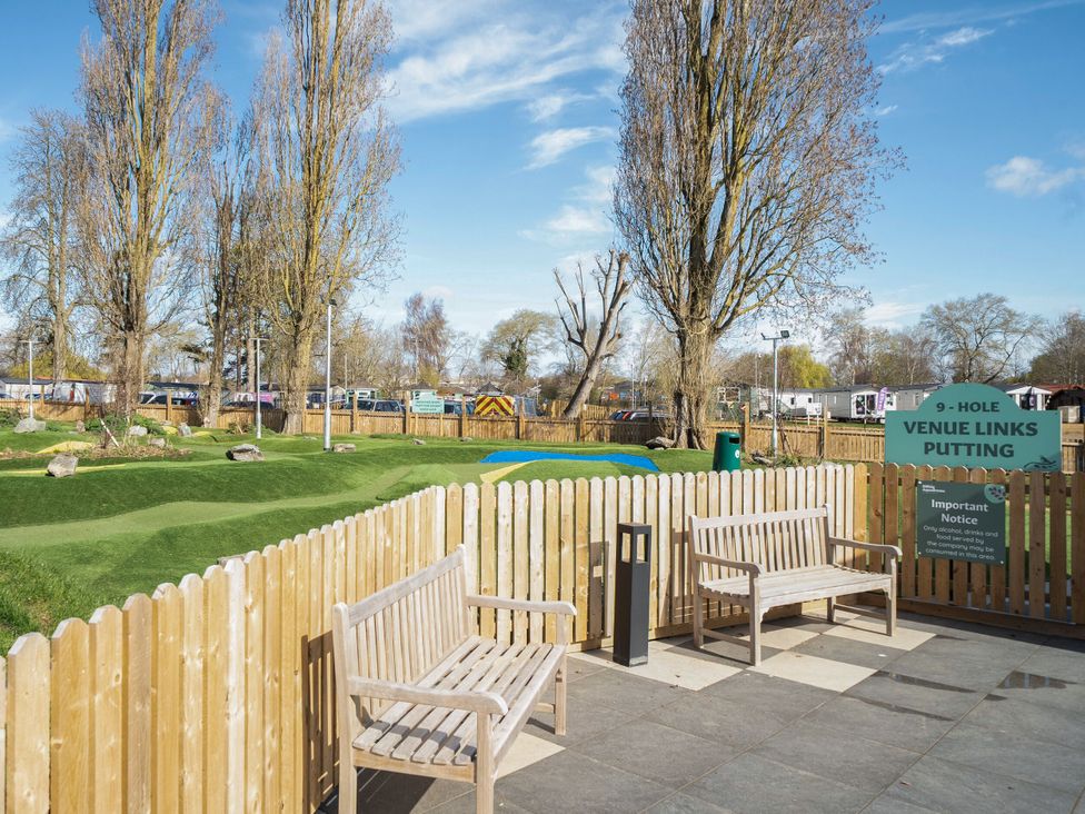 A fenced outdoor area with two wooden benches overlooking a 9-hole putting green at Billing Aquadrome Holiday Park