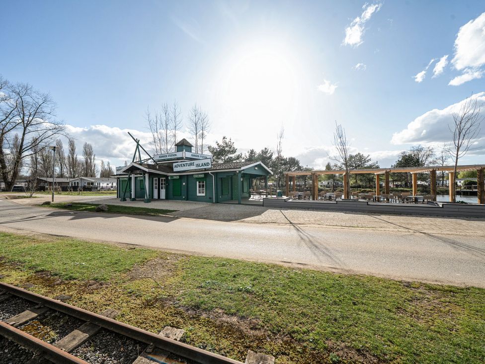 An outdoor view of a green building with signs reading Adventure Island and Ranger Station near railway tracks and a seating area at Billing Aquadrome Holiday Park