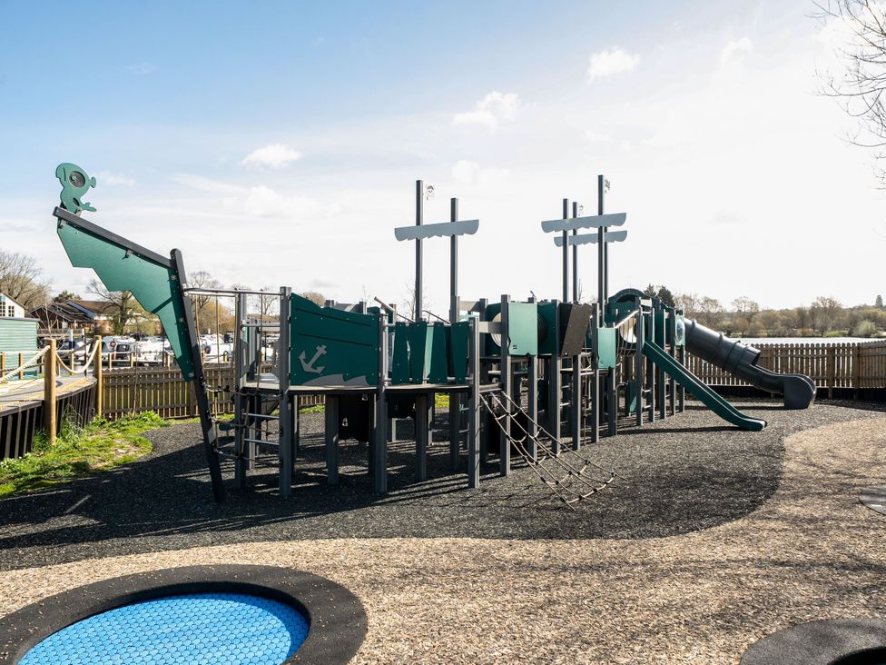 A playground with a pirate ship climbing frame and slides near a fenced area at Brookside Bliss - Billing Aquadrome Holiday Park