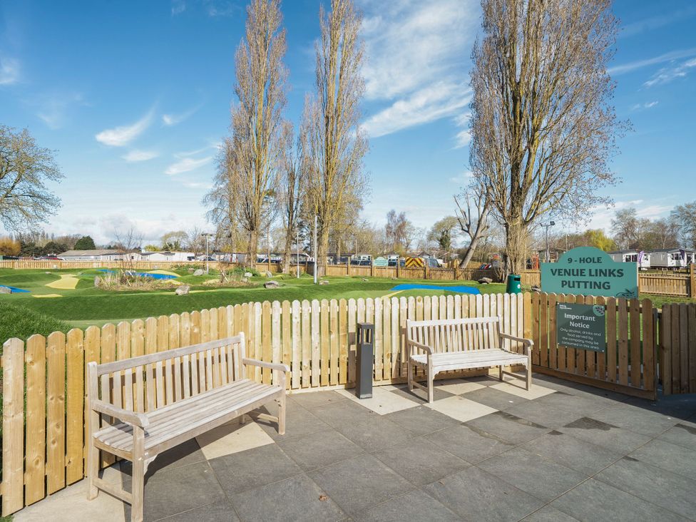 An outdoor area with two wooden benches and a fenced 9 hole putting green at Brookside Bliss - Billing Aquadrome