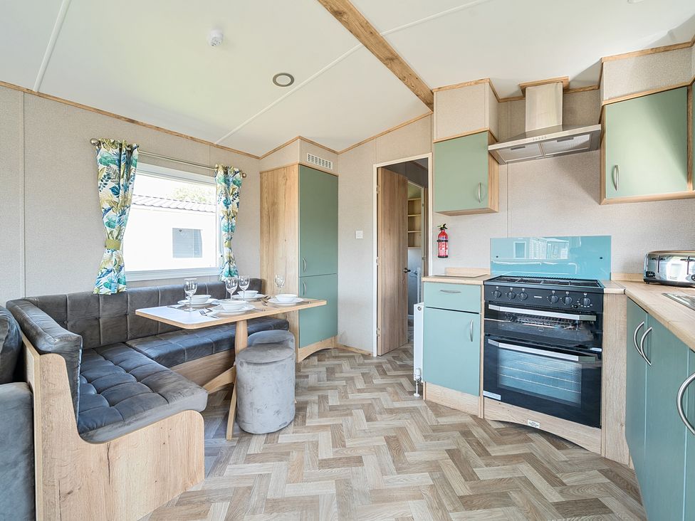 A kitchen and dining area with green cabinets a stove and a corner sofa with a table at Brookside Bliss - Billing Aquadrome in Billing Aquadrome Holiday Park