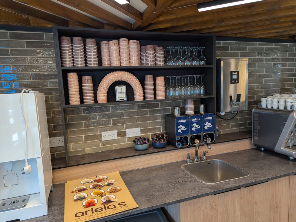 A coffee station with paper cups glassware coffee pods and a sink at Brookside Bliss - Billing Aquadrome in Billing Aquadrome Holiday Park