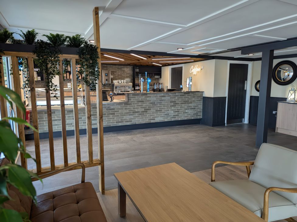 An indoor cafe area with a coffee counter a wooden table and chairs and plants at Brookside Bliss - Billing Aquadrome Holiday Park