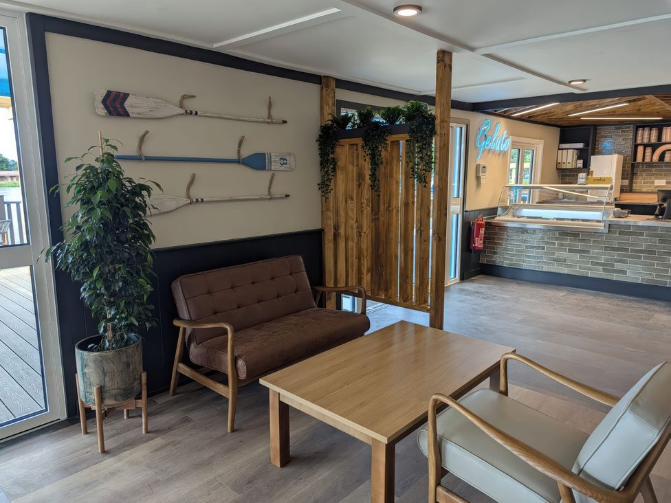 A seating area with a brown sofa, beige armchair, wooden coffee table, decorative oars on wall and gelato counter at Brookside Bliss - Billing Aquadrome