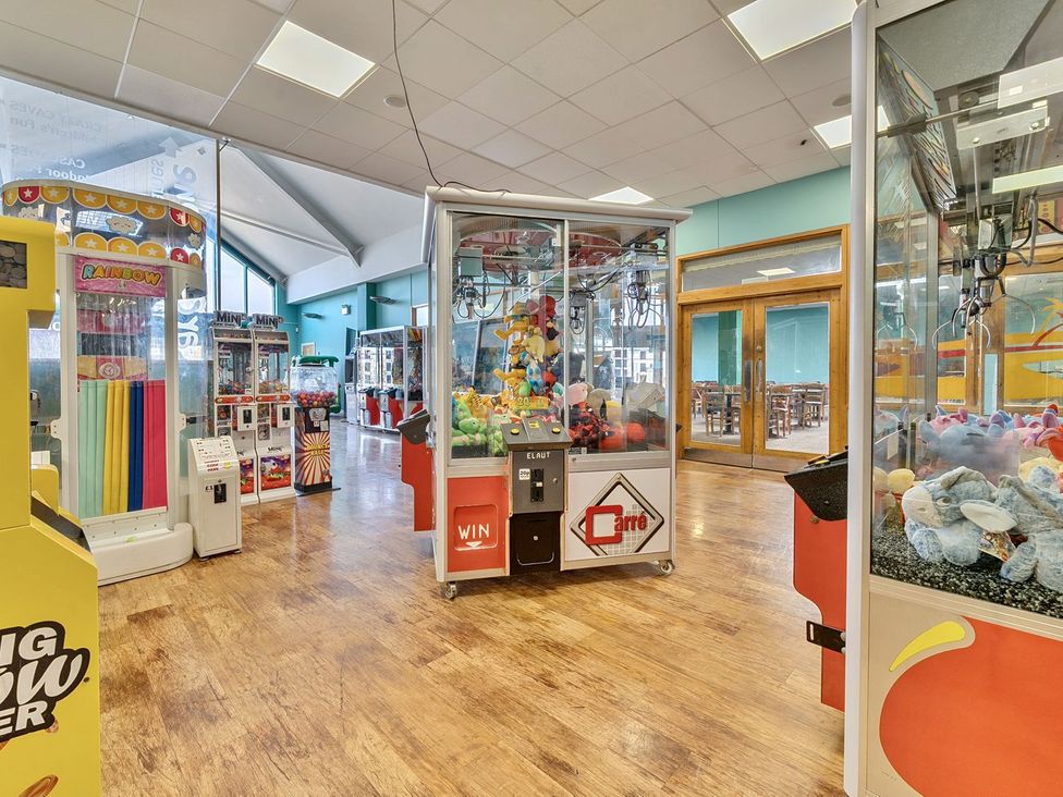An arcade room with claw machines and prize games with tables visible through glass doors at Mariners Meadow  Hayling Island Holiday Park