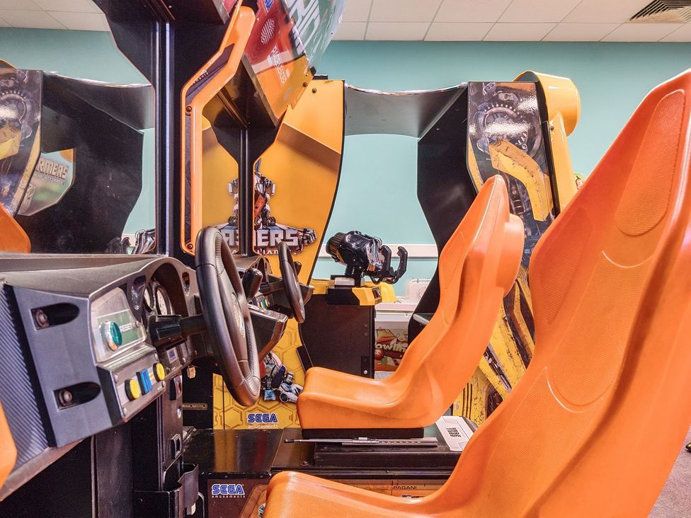 An arcade room with orange seats and steering wheels in front of game consoles at Mariner's Meadow - Hayling Island in Hayling Island Holiday Park