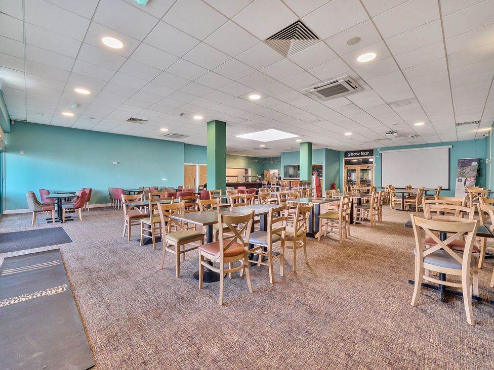 A dining area with multiple wooden tables and chairs a bar and a projector screen at Mariners Meadow Hayling Island Holiday Park