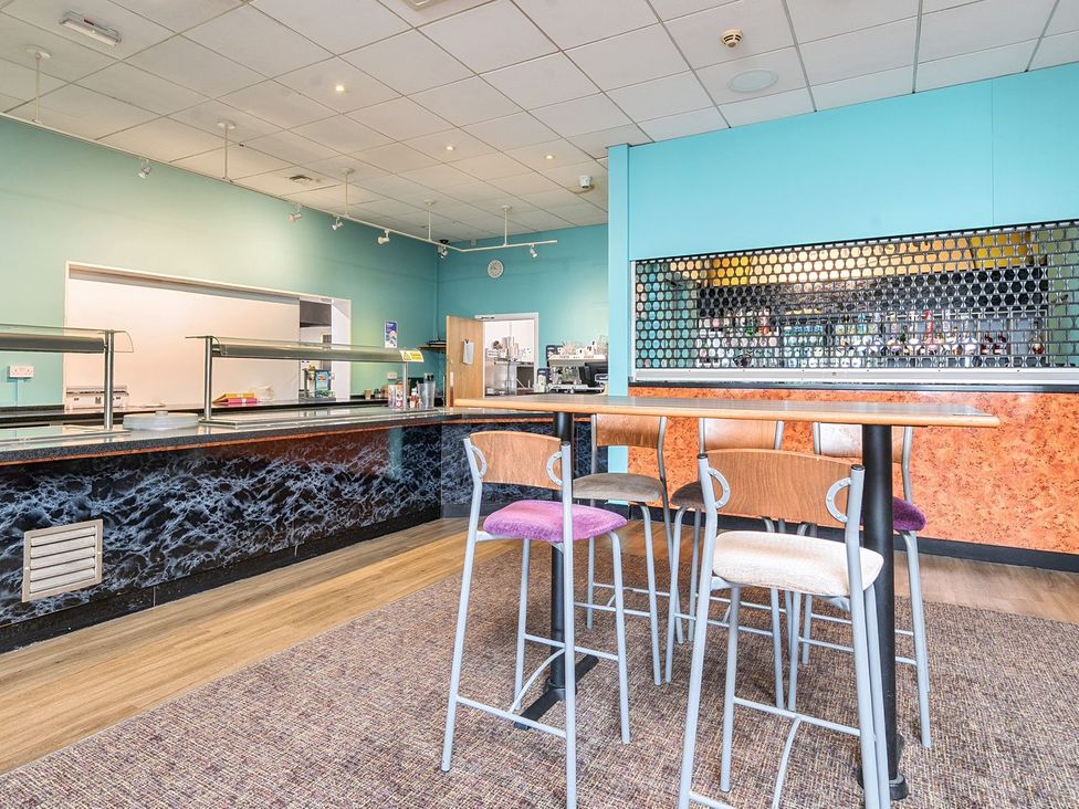 A room with high tables and chairs next to a serving counter and a bar area at Mariners Meadow Hayling Island