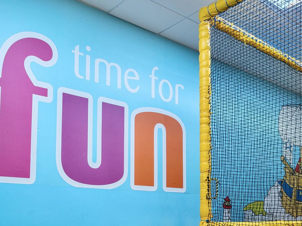 A blue wall with time for fun text next to a yellow netted play area at Mariner's Meadow - Hayling Island in Hayling Island Holiday Park