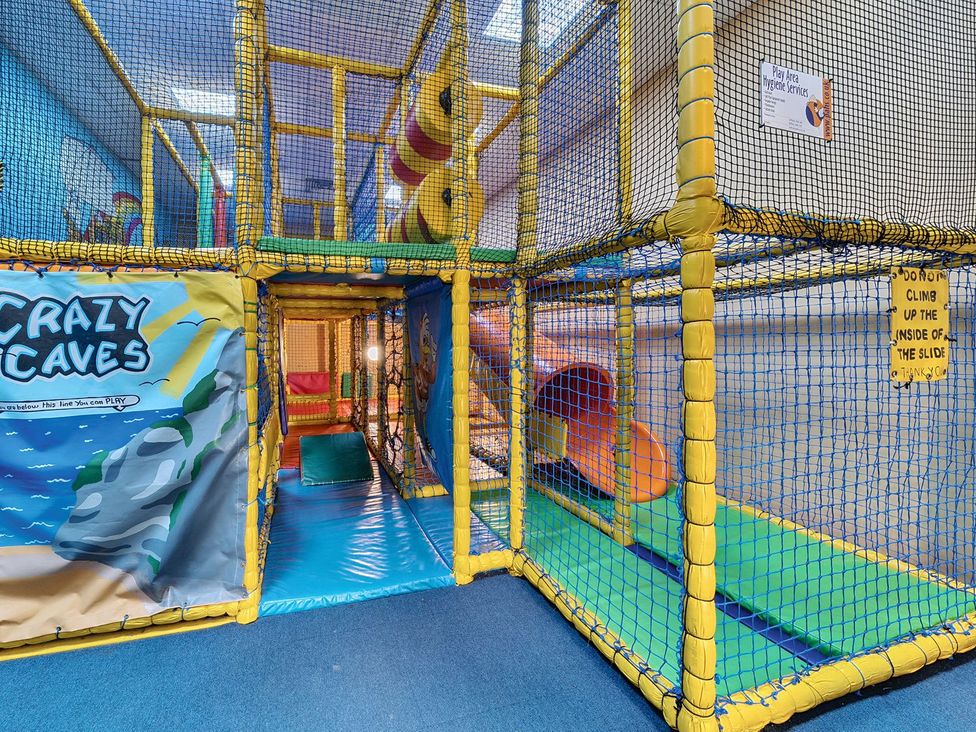 An indoor children's play area with climbing structures slides and padded flooring at Mariners Meadow Hayling Island Holiday Park