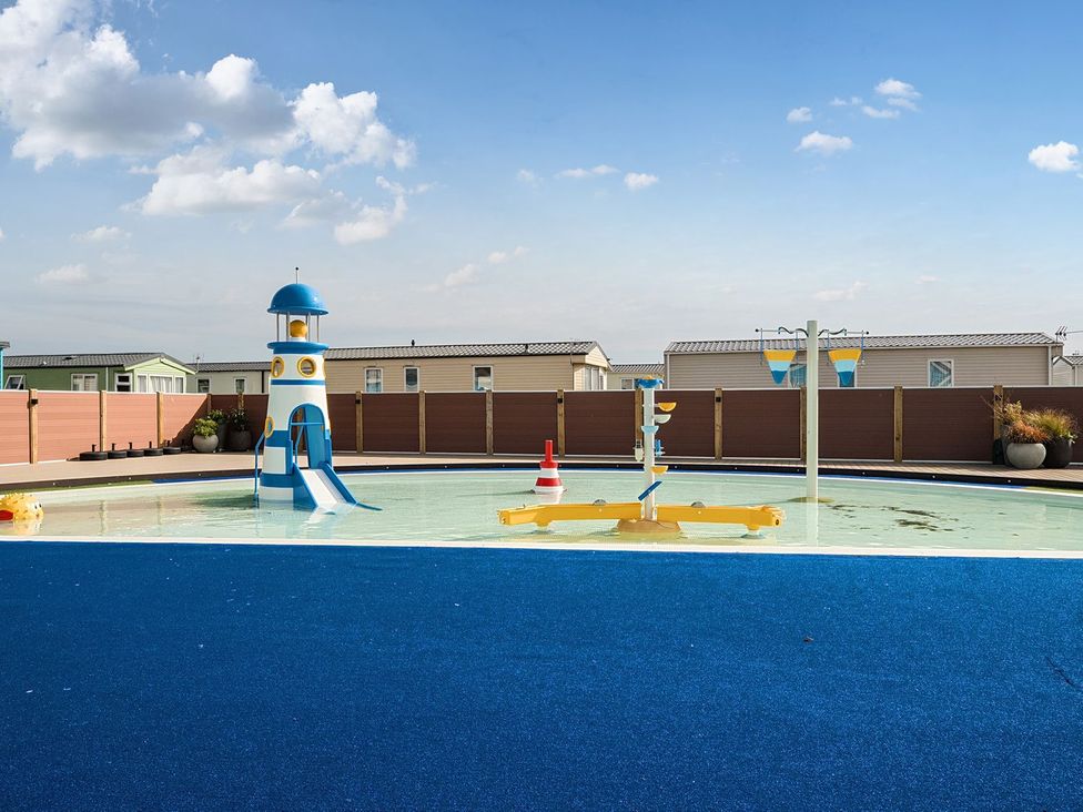 An outdoor children's splash pool with a blue and white lighthouse slide and water play features at Mariner's Meadow - Hayling Island in Hayling Island Holiday Park