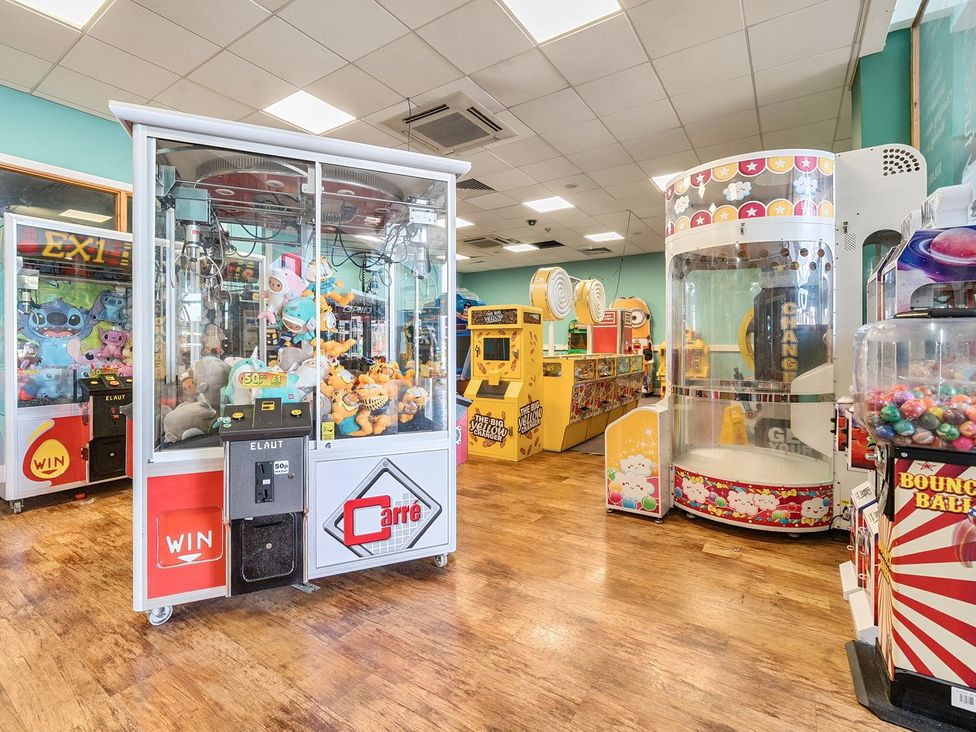 An arcade room with claw machines and candy dispensers on a wooden floor at Seaside Serenity - Hayling Island Holiday Park