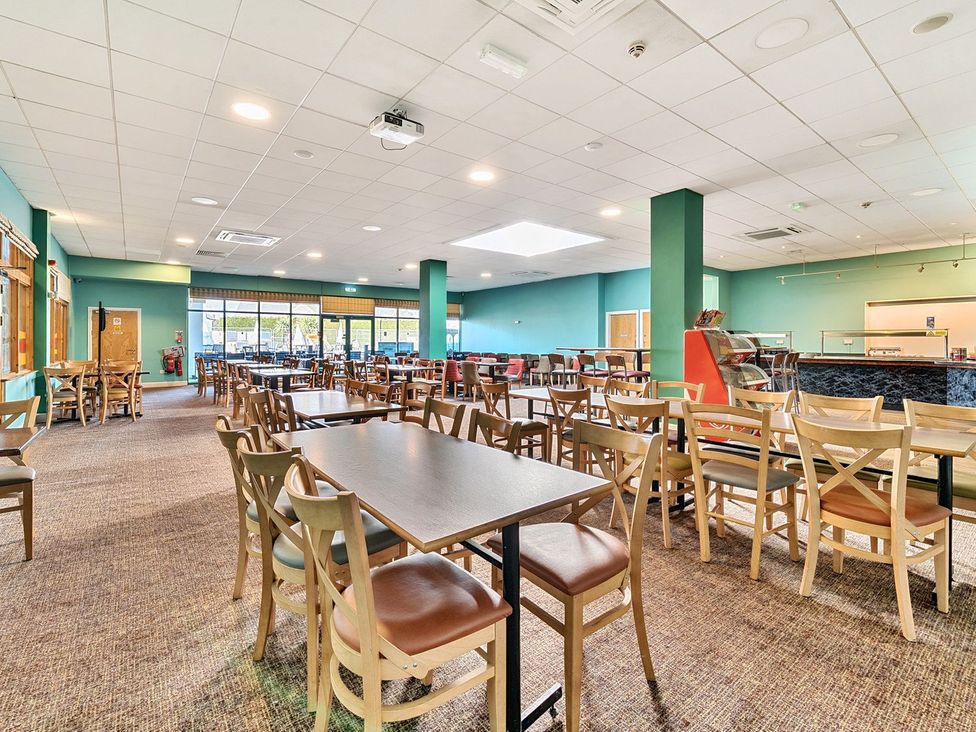A dining area with multiple tables and chairs in a large room with teal walls and ceiling lights at Seaside Serenity - Hayling Island in Hayling Island Holiday Park