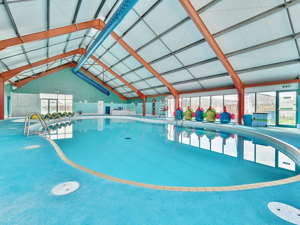 An indoor swimming pool with blue flooring and a sloped ceiling at Seaside Serenity - Hayling Island Hayling Island Holiday Park