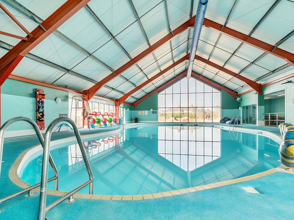 An indoor swimming pool with metal ladders and large windows at Seaside Serenity - Hayling Island in Hayling Island Holiday Park