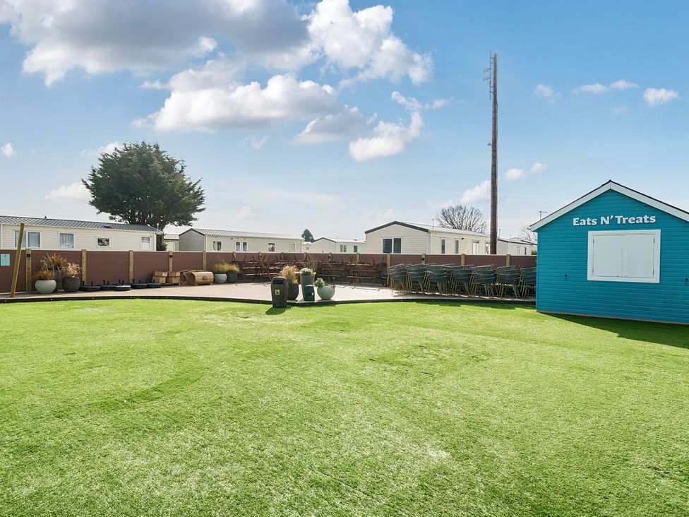 A grassy outdoor area with stacked chairs and tables near a blue building labeled Eats N Treats at Seaside Serenity - Hayling Island Hayling Island Holiday Park