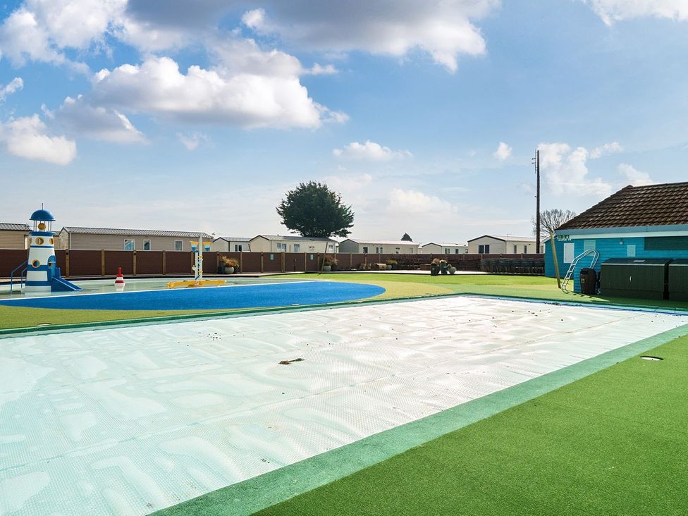 An outdoor pool area with a children's play pool and a slide near mobile homes at Seaside Serenity - Hayling Island in Hayling Island Holiday Park