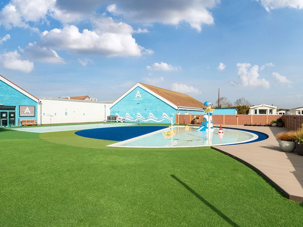 An outdoor pool area with a shallow children's pool and blue buildings in the background at Seaside Serenity - Hayling Island in Hayling Island Holiday Park