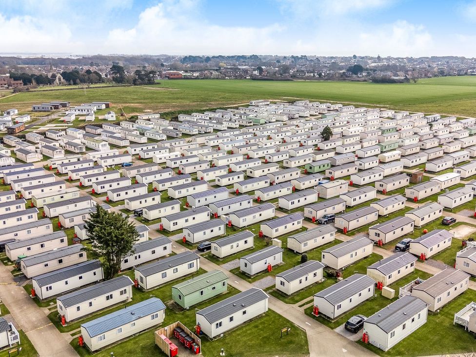 An aerial view of rows of beige and green mobile homes on a grassy area with a town and fields in the background at Seaside Serenity - Hayling Island in Hayling Island Holiday Park