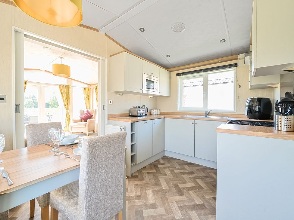 A kitchen with a dining table and chairs next to a living area with an armchair and windows at Seaside Serenity - Hayling Island in Hayling Island Holiday Park