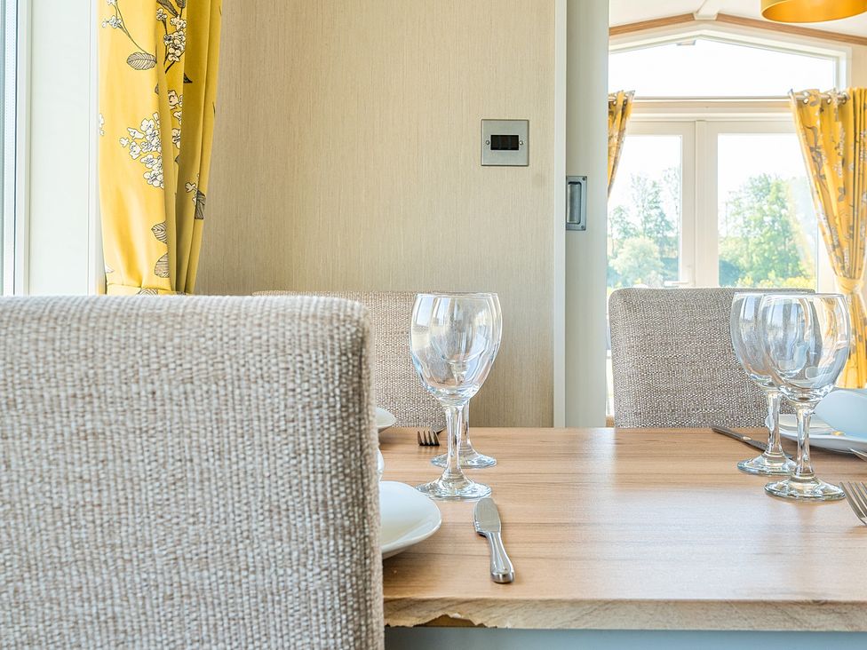 A dining table set with wine glasses plates and cutlery beside windows with yellow floral curtains at Seaside Serenity - Hayling Island in Hayling Island Holiday Park