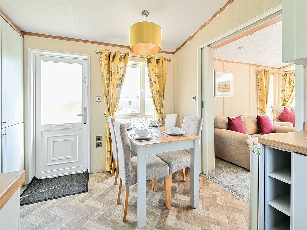 A dining area with a table set for four next to yellow floral curtains and a door with an adjacent living room at Seaside Serenity - Hayling Island in Hayling Island Holiday Park