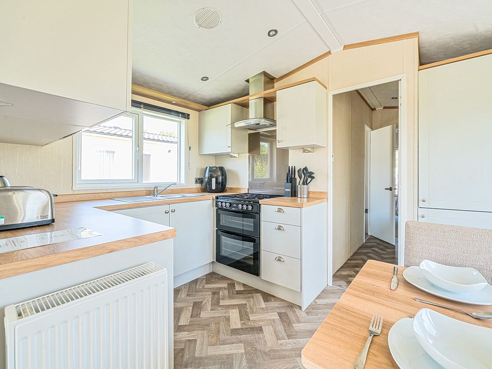 A kitchen with a stove toaster air fryer sink and dining table with plates and cutlery at Seaside Serenity - Hayling Island in Hayling Island Holiday Park
