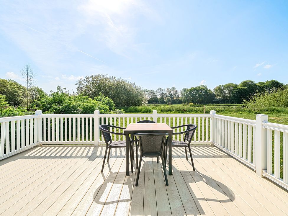 A wooden deck with a square table and four chairs overlooking greenery and trees at Seaside Serenity - Hayling Island in Hayling Island Holiday Park