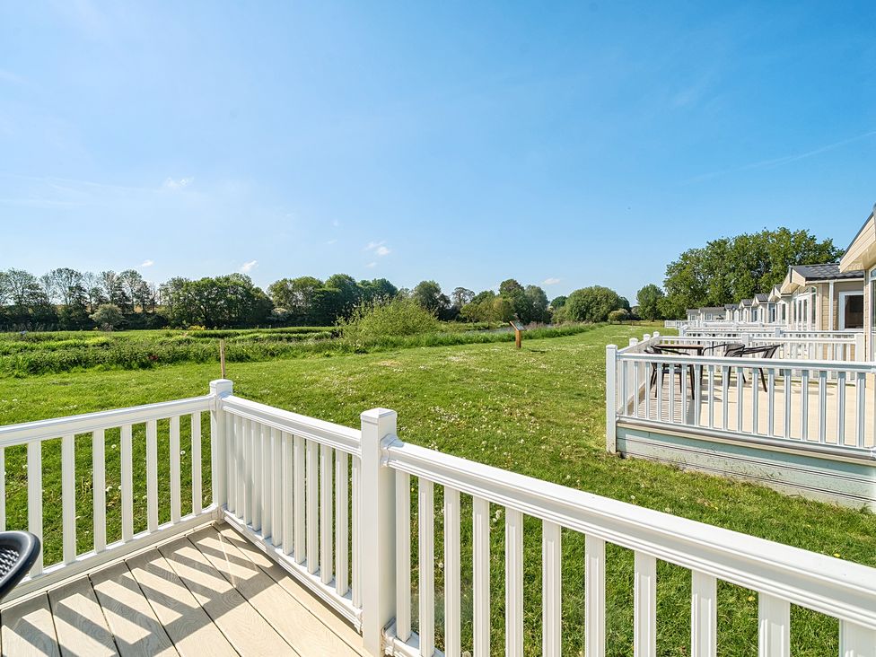 A view from a deck with white railing overlooking a grassy field and row of mobile homes at Seaside Serenity - Hayling Island in Hayling Island Holiday Park