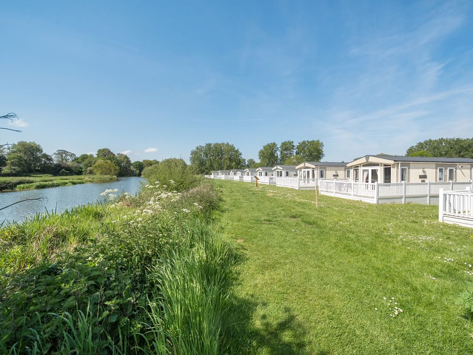 A row of holiday lodges next to a river with grass and trees at Seaside Serenity - Hayling Island in Hayling Island Holiday Park