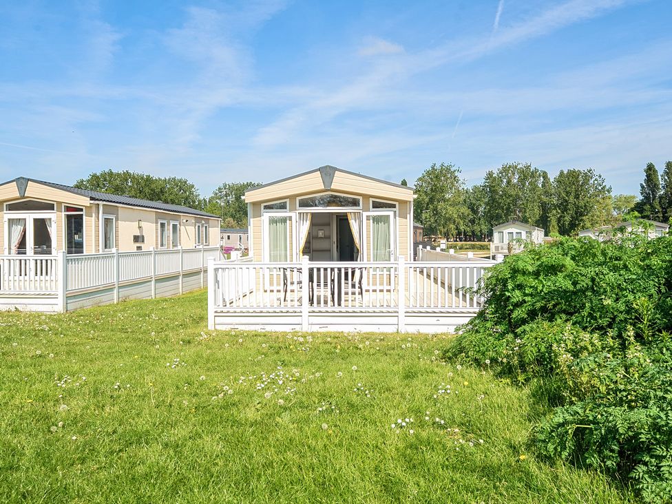A mobile home with a white railing and patio furniture on a grassy area at Seaside Serenity - Hayling Island in Hayling Island Holiday Park