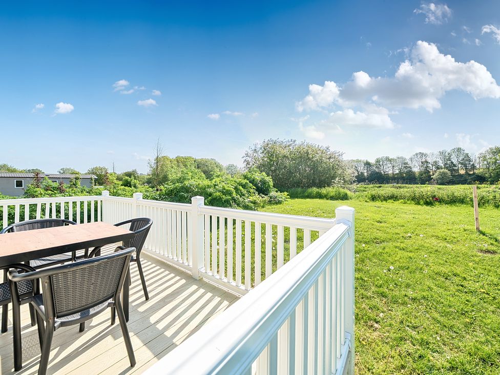 An outdoor deck with a table and four chairs overlooking a grassy field and trees at Seaside Serenity - Hayling Island Hayling Island Holiday Park