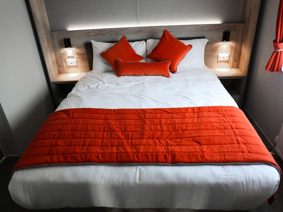 A bedroom with a bed and orange cushions at Sandy Shores - Hayling Island