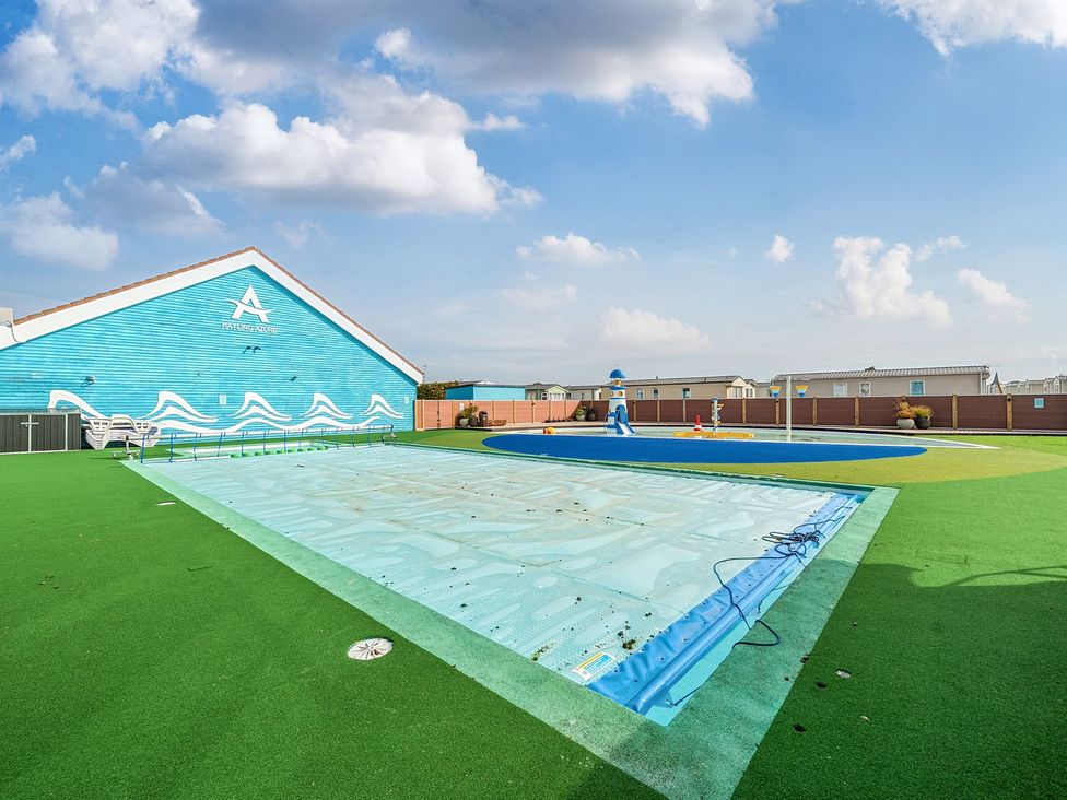 An outdoor pool area with a covered swimming pool and a children's splash pad near a blue building at Island Breeze - Hayling Island in Hayling Island Holiday Park