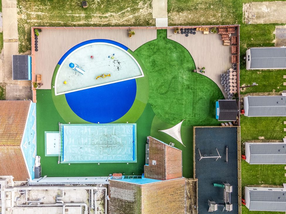 An aerial view of a playground with a circular splash pad a rectangular pool a swing set and several small cabins at Island Breeze - Hayling Island in Hayling Island Holiday Park