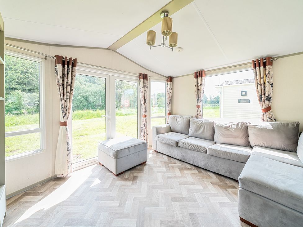 Living room with large gray sectional sofa ottoman and windows with floral curtains at Island Breeze - Hayling Island Hayling Island Holiday Park