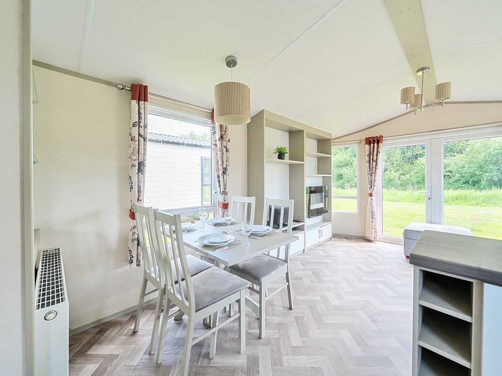 A dining area with a table set for four chairs next to large windows and a built in shelving unit at Island Breeze - Hayling Island in Hayling Island Holiday Park