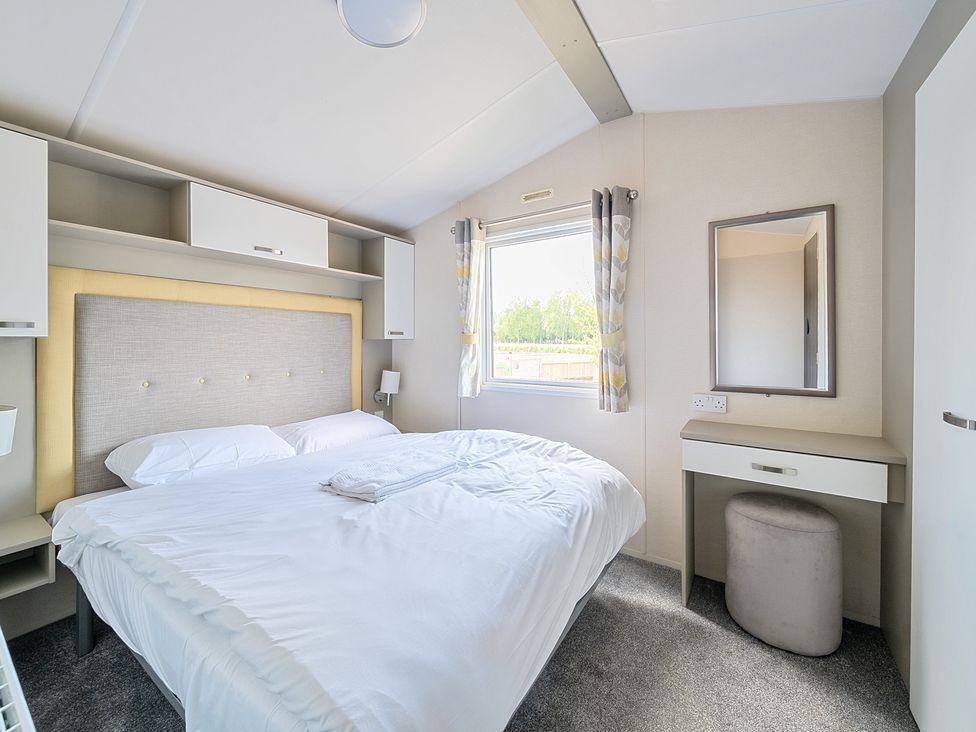 A bedroom with a double bed a window with curtains and a vanity table with a mirror at Island Breeze - Hayling Island in Hayling Island Holiday Park