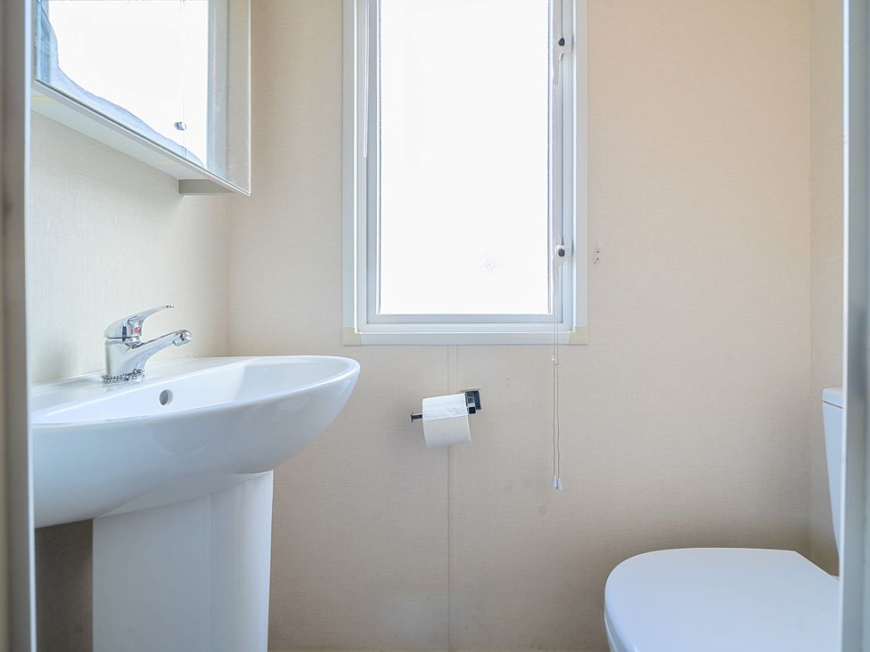 A small bathroom with a sink a window a toilet and a toilet paper holder at Island Breeze - Hayling Island Hayling Island Holiday Park