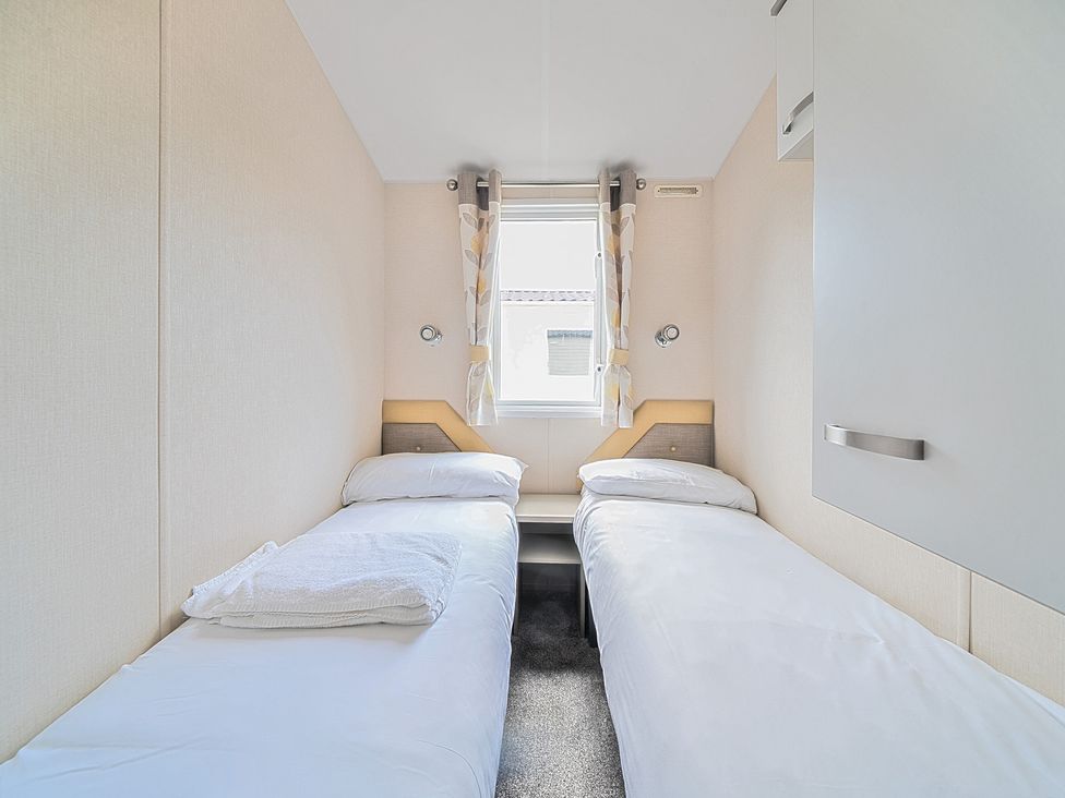 A small bedroom with two single beds separated by a small table and a window with curtains at Island Breeze - Hayling Island in Hayling Island Holiday Park